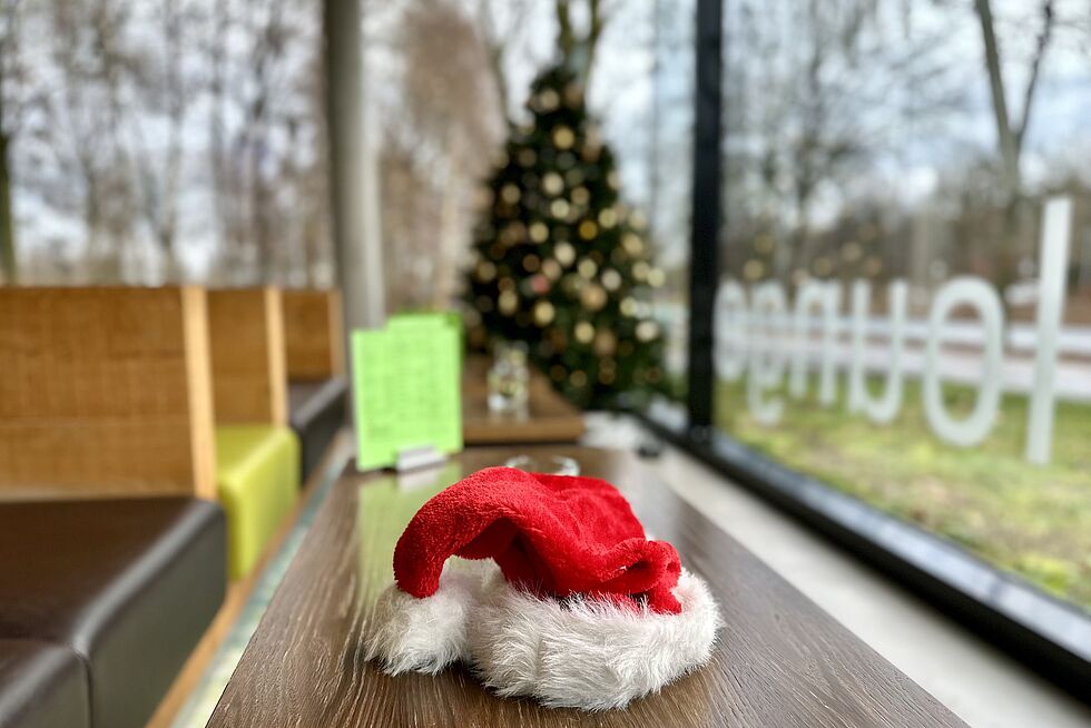 Weihnachtsmütze liegt auf einem Tisch vor einem beleuchteten Weihnachtsbaum.
