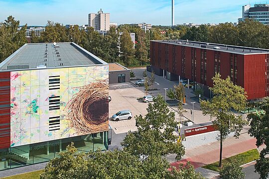 Luftaufnahme auf zwei große Gebäude wobei auf einem ein überdimensionales Nest an der Fassade angebracht ist