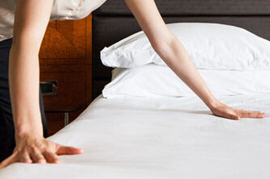 Maid making a bed with white sheets
